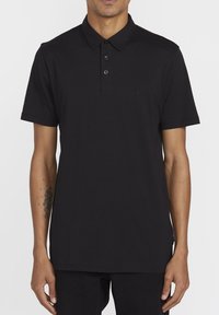 Sort polo-shirt lavet af bomuld, med en tre-knaps placket, korte ærmer og et lille logo på venstre bryst. Glat tekstur.