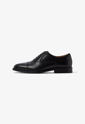 Chaussure Oxford pour homme en cuir noir avec des détails brogués et un laçage fermé, vue du côté extérieur sur un fond blanc.