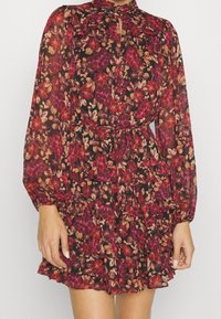 Blumenkleid mit Rüschenstufen, langen Ärmeln, hohem Kragen, dunklem Hintergrund und roten, rosa sowie cremefarbenen Blumenmustern.