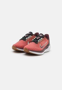 Scarpe da corsa Nike in rosso e borgogna con tomaia in tessuto testurizzato, lacci neri e suola in gomma. Presentano uno swoosh argento e accenti menta.
