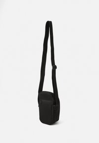 Borsa a tracolla nera realizzata in tessuto con una superficie texturizzata, dotata di una tasca anteriore con zip e di una tracolla regolabile.