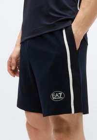 Tmavomodré šortky s bielym bočným pruhom. Na nohavici má nášivku s logom. Strih so vreckami, navrhnutý pre pohodlie a pohyblivosť.