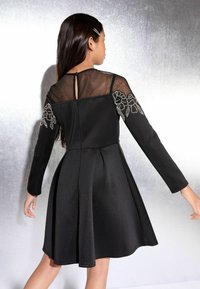 Fekete A vonalú ruha hosszú ujjakkal, átlátszó hálós dekoltázzsal és virágos hímzéssel a vállakon. Simaság érzetű anyag, harang alakú szegés, hátul zippzáras záródás.