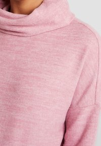 Jasnoróżowy sweter z pulowerem wykonany z miękkiego dzianinowego materiału, z luźnym dekoltem typu cowl oraz bezszwowymi ramionami dla swobodnego kroju.