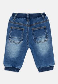 Vista trasera de unos pantalones jogger de mezclilla azul para niño pequeño con cintura elástica, dos bolsillos traseros y puños acanalados en los tobillos.