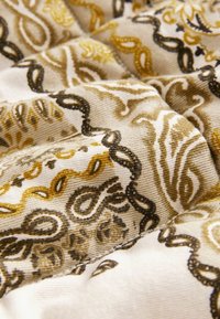 Tissu beige avec des motifs cachemire marron et jaune, présenté en gros plan avec des plis texturés et des coutures visibles.