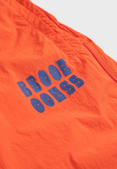 Tissu orange vif avec un texte graphique bleu présentant des lettres déformées et une couture diagonale près du bord d'une poche zippée.