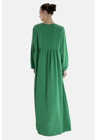 Długa zielona sukienka z lekkiego materiału, z długimi rękawami, luźnym krojem i marszczonym stanem. Gładka faktura z płynną sylwetką.