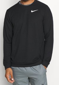 Sudadera negra de tela suave, con cuello redondo y mangas largas, presenta un logo blanco de Nike en la parte superior del pecho izquierdo.