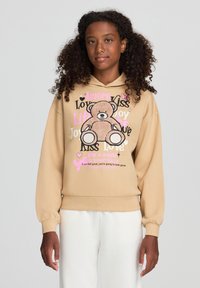 Felpa beige con una grafica di un orsetto e testo colorato. Presenta polsini e orlo a costine, tessuto morbido e vestibilità comoda.