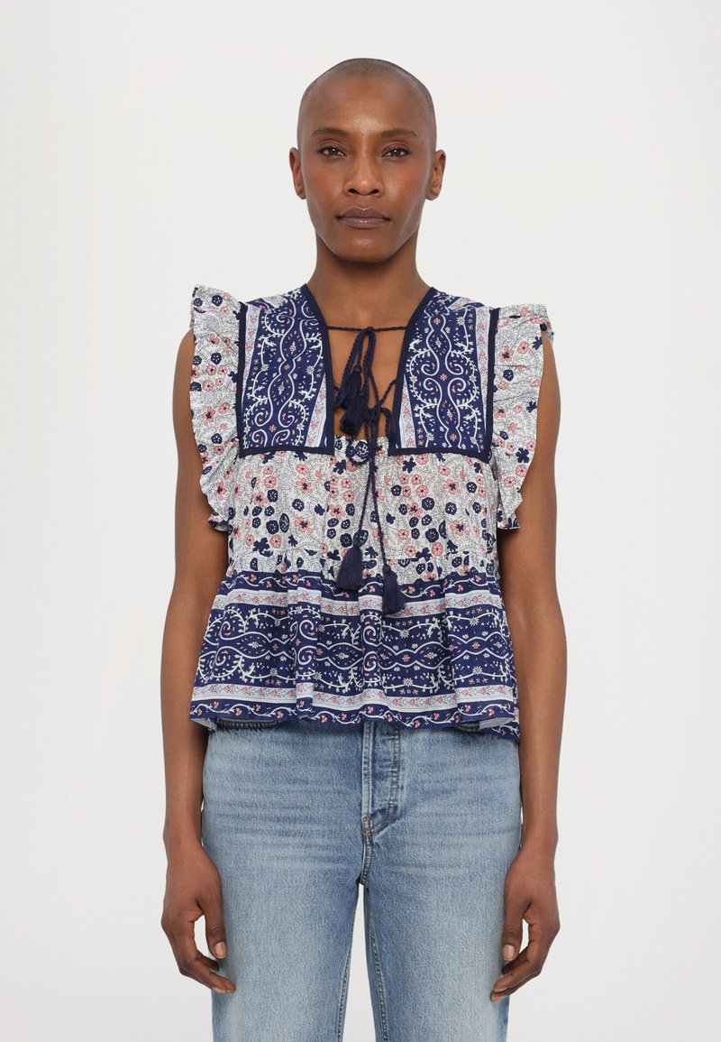 Blusa de patrón azul y blanco con mangas con volantes, que presenta un escote con cordón y motivos florales, superpuesta con rayas horizontales.