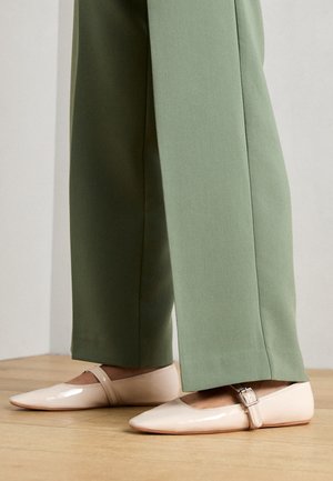 Lysrosa patentlæderballerinaer med spids tå og ankelrem, parret med løstsiddende, lysegrønne bukser. Glat tekstur, minimal detaljer.