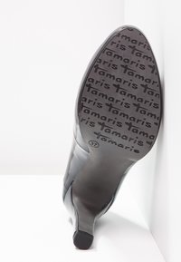 Chaussure à talon haut noire avec une tige lisse, un nez pointu et une semelle en caoutchouc texturée embossee avec "Tamaris." Taille marquée comme 37.