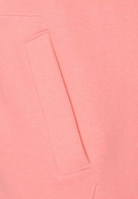 Light pink hoodie fabric close-up with a ribbed pocket detail. Soft texture and smooth surface, highlighting the material's stretch and weight.