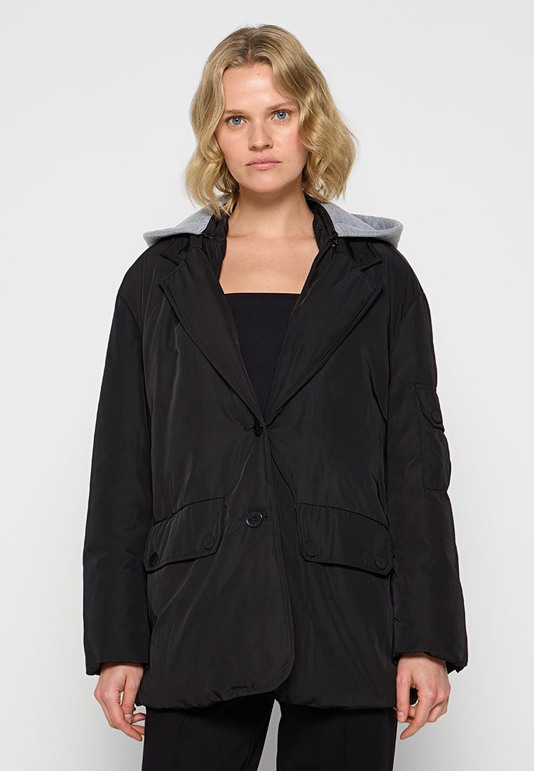 Schwarze gepolsterte Jacke mit einer grauen Kapuze, ausgestattet mit einem Knopfverschluss und Fronttaschen. Glattes Material, oversized Passform und lange Ärmel.