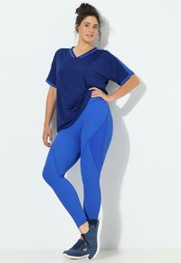 Granatowy, luźny sportowy top z dekoltem w serek, połączony z dopasowanymi legginsami w kolorze kobaltowym, zdobionymi fakturowanymi szwami i akcentami.