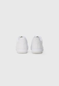 Nike Air sneakers bianche, tomaia in pelle, design a basso profilo, suola testurizzata, colletto imbottito e branding discreto sul tallone.
