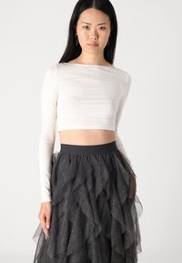 Bílé dlouhé rukávy cropped top spárované s černou sukní z tylu s volány, která má stříbrné puntíky a přiléhavý pas.