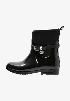 Botín de lluvia negro brillante hasta el tobillo con sección superior mate, correa decorativa con hebilla y pequeño charm redondo con logo en el lateral.