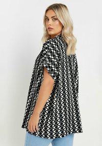 Camicia a maniche corte a zigzag in bianco e nero con una vestibilità ampia, dotata di un collo alto e un orlo leggermente curvo.
