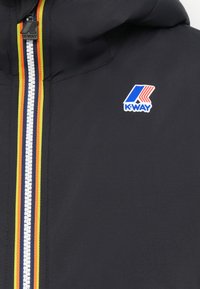 Veste noire avec capuche, dotée d'une fermeture éclair avec une bande multicolore. Comprend un logo bleu et rouge en haut à gauche.