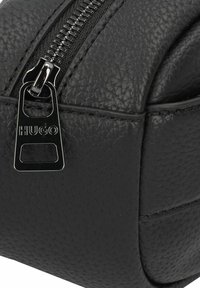 Pochette in pelle nera texturizzata con cerniera argentata. Presenta un tirazip brandizzato con "HUGO" inciso. Forma rettangolare compatta.