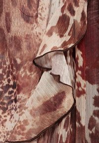 Tissu léger et fluide dans des nuances de brun et de crème avec un motif tacheté, présentant des bords volantés et une texture délicate.