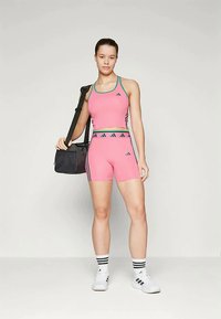 Roza sportska kratka majica i kratke hlače s tirkiznim akcentima; crna sportska torba u ruci; bijele čarape s crnim prugama i bijeli tenisice.