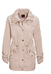 Lichtbeige jas gemaakt van gestructureerde stof. Beschikt over een trekkoord in de taille, gouden accenten, een rits aan de voorkant en knoopzakken.