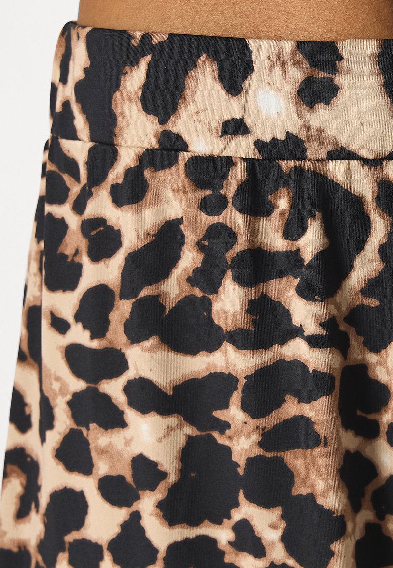 Tissu imprimé léopard présentant un mélange de couleurs noir et fauve avec une texture lisse. Le design comprend des taches irrégulières et une taille froncée.