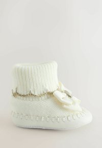 Valge kudumiga saabas ribatud varruka ja hõbedase ketiga, millel on valge pael. Pehme tekstuur, sile tald ja dekoratiivne õmblus.