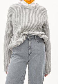 Suéter gris de canalé con un escote amplio, combinado con jeans de mezclilla claros de cintura alta. La textura de la tela es suave y de corte holgado.
