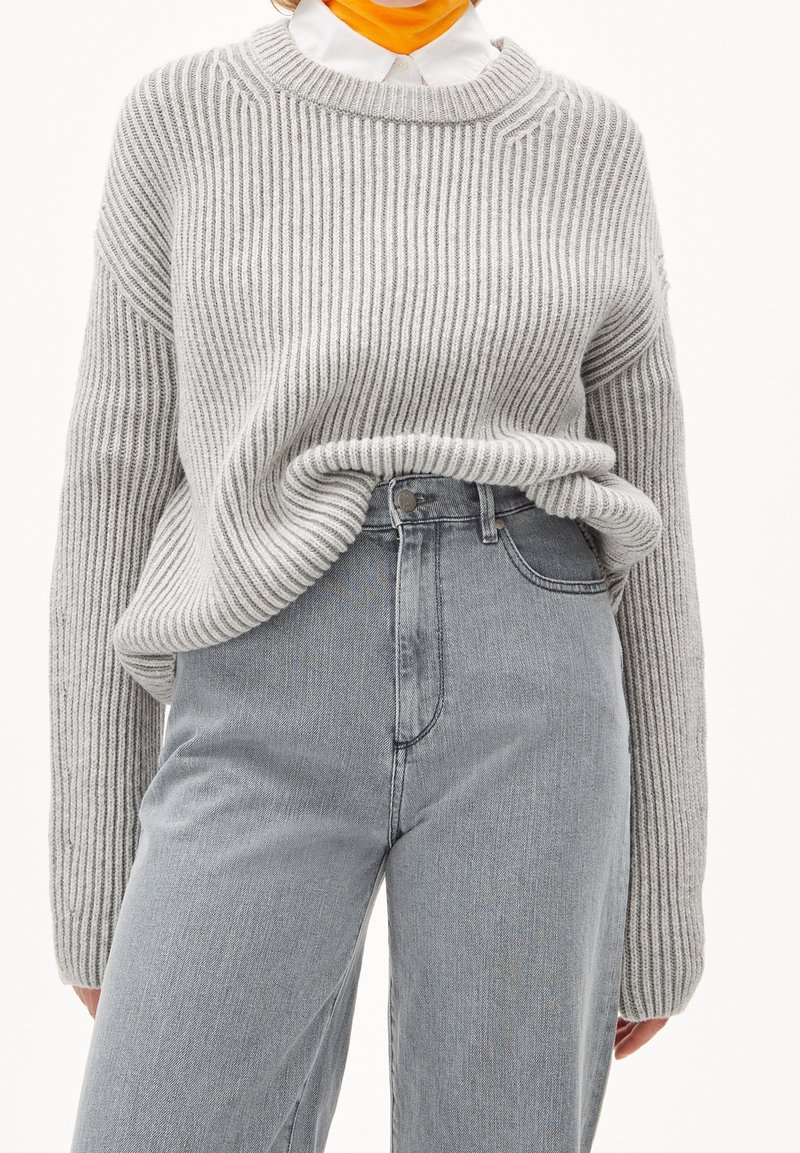 Suéter gris de canalé con un escote amplio, combinado con jeans de mezclilla claros de cintura alta. La textura de la tela es suave y de corte holgado.