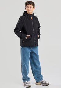 Black hooded jacket with a zipper, featuring side pockets and orange accents, paired with loose blue denim jeans and gray sneakers.