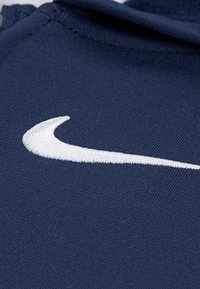 Tissu marine avec une texture douce, ornée d'un logo Swoosh Nike brodé en blanc, positionné dans la partie supérieure.