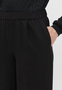 Pantalons noirs au tissu lisse, dotés de poches latérales et d'une taille élastique, conçus pour un usage décontracté et le confort.