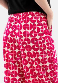 Pantaloni rosa a fantasia con cerchi geometrici su uno sfondo crema, dotati di una vita elastica e tasche laterali.