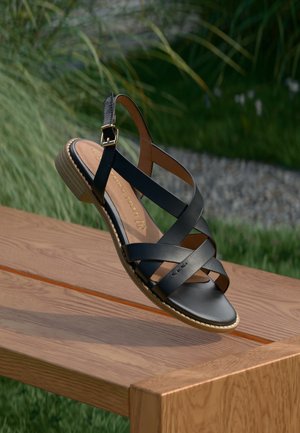 Sandale en cuir noir avec des brides croisées, sangle de cheville ajustable et un talon bas texturé. Dotée d'une semelle intérieure beige et de détails de marque.