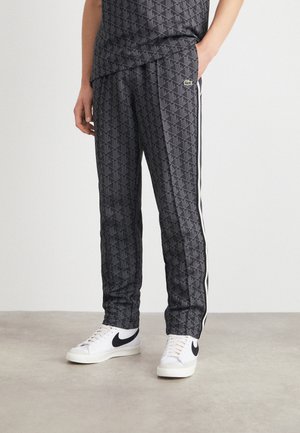 Person trägt schwarze Trainingshose mit weißen Seitenstreifen und weiße Sneaker mit schwarzen Swoosh-Logos.