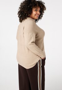 Beige trui in zachte brei, met een licht oversized pasvorm en lange mouwen, gecombineerd met donkerbruine broek met gestreepte zijstrepen.