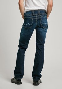 Mørkeblå denimjeans med rett ben-design, som har to baklommer med bølgete stikninger og et klassisk liv.