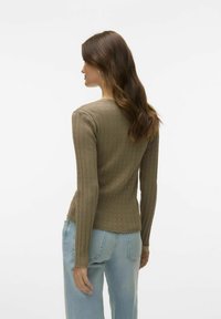 Olivgrön ribbad stickad långärmad topp med en figurnära design och vågig fåll, kombinerad med ljusblå högmidjade jeans.