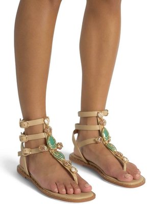 Sandales plates beiges avec plusieurs brides autour de la cheville, ornées de pierres précieuses turquoise et rose, d'une semelle intérieure texturée et d'une semelle profil basse.
