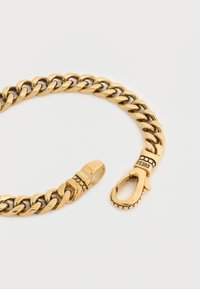 Βραχιόλι αλυσίδας από μεταλλικό υλικό σε χρυσή απόχρωση με διασταυρούμενους κρίκους, υφή κλεισίματος και εμφανές λογότυπο στη μεταλλική σύνδεση.