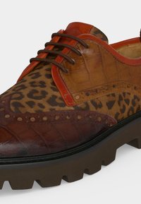 Chaussure habillée à lacets pour homme avec tissu à motif léopard, panneaux en cuir marron et beige, détails brogue, et semelle épaisse noire et robuste.