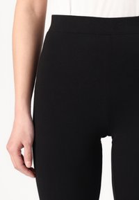 Zwarte leggings van rekbaar materiaal met een hoge tailleband, met een gladde textuur en zonder zichtbare patronen of hardware-details.