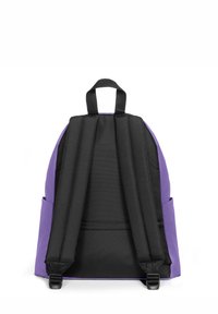 Mochila púrpura con correas y acentos negros. Cuenta con un asa superior, correas de hombro acolchadas y bolsillos laterales negros. Textura de tela suave.