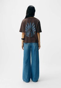 Bruine oversized t-shirt met blauw grafisch ontwerp van handen en zon. Gecombineerd met blauwe wijde broek met stiksels op de achterzak.