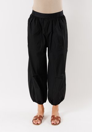 Pantaloni neri con elastico in vita, dalla vestibilità ampia e con polsini arricciati. Realizzati in tessuto morbido, con più tasche e una superficie liscia.