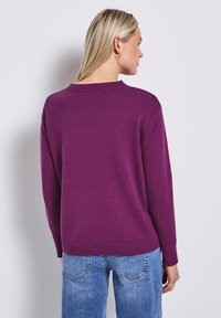 Lila tröja med rund halsringning, långa ärmar och ribbade manschetter, kombinerad med ljusblå jeans. Slät textur, avslappnad passform.